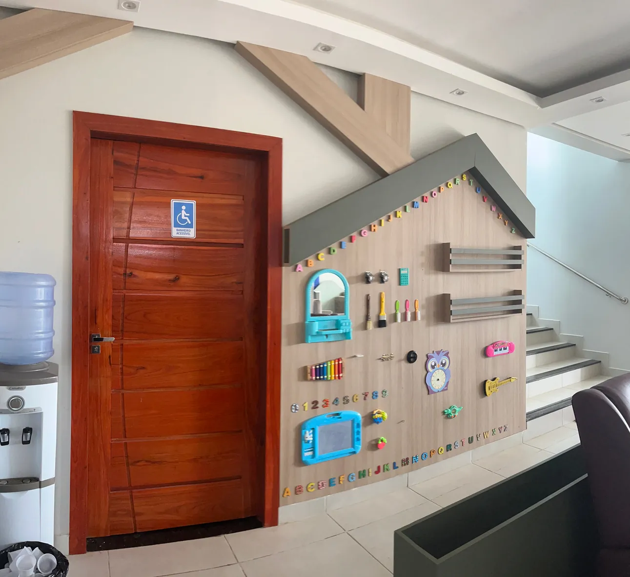 Painel sensorial da recepção, em formato de casinha, com letras, números, espelho, xilofone e brinquedos presos na parede