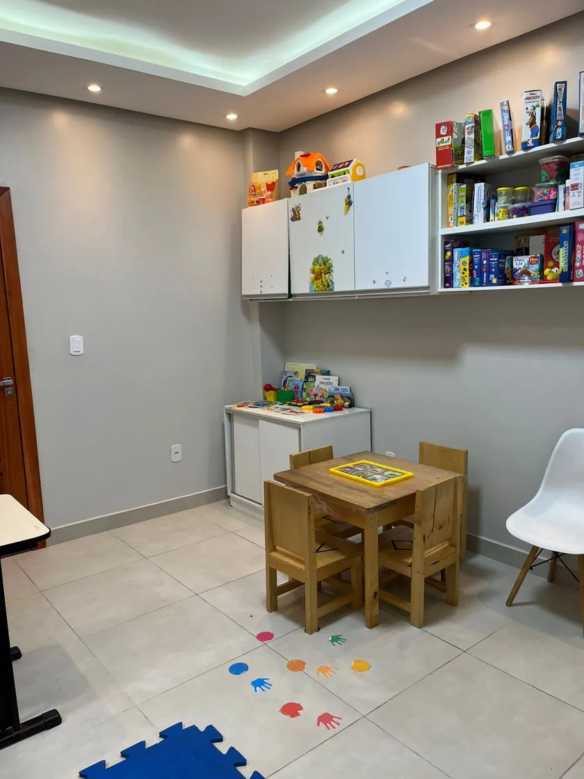 Sala individual com mesinha e cadeiras de madeira, estantes de jogos e mãos coloridas coladas no chão